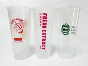 Disposable plastic cups with beverage branding, featuring bubble tea graphics and text in red and green, printed by the AP-600-8 Automatic Cup Printing Machine. Demonstrates multi-color printing precision and LED UV curing for disposable beverage packaging.