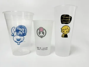 Disposable plastic cups with vibrant multi-color beverage designs, including a cow logo and bubble tea character, printed by the AP-600-8 Vertical Rotary Screen Printing Machine. Showcases corona pre-treatment for enhanced ink adhesion on disposable cups.